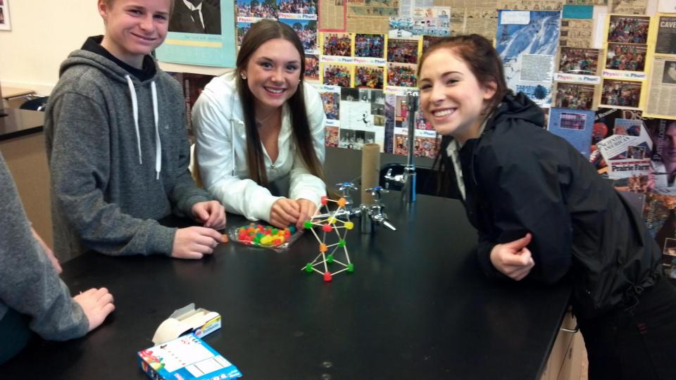 Three students smiling in a science classroom.